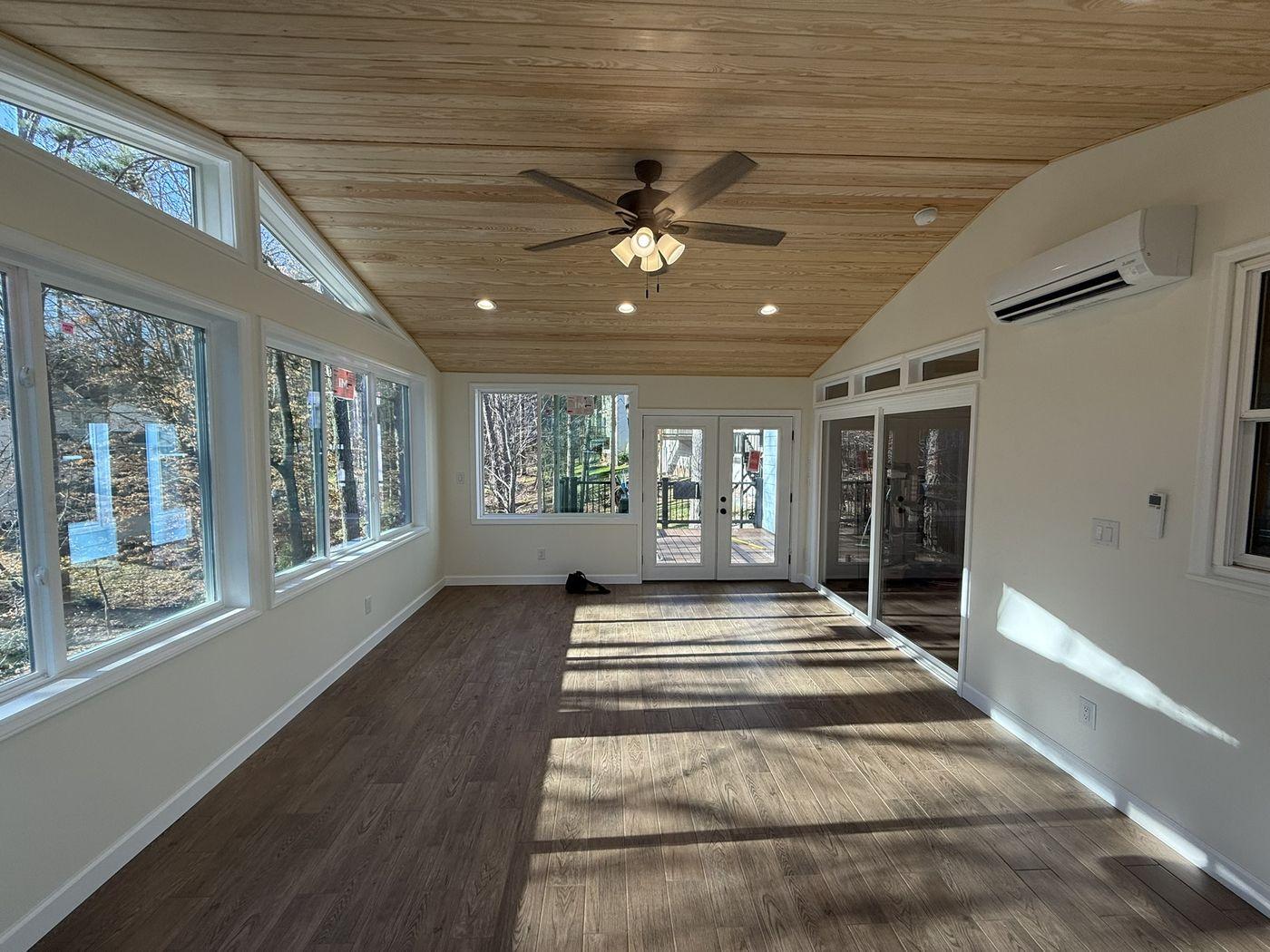 Completed sunroom addition interior with a tongue-and-groove pine ceiling and full window wall