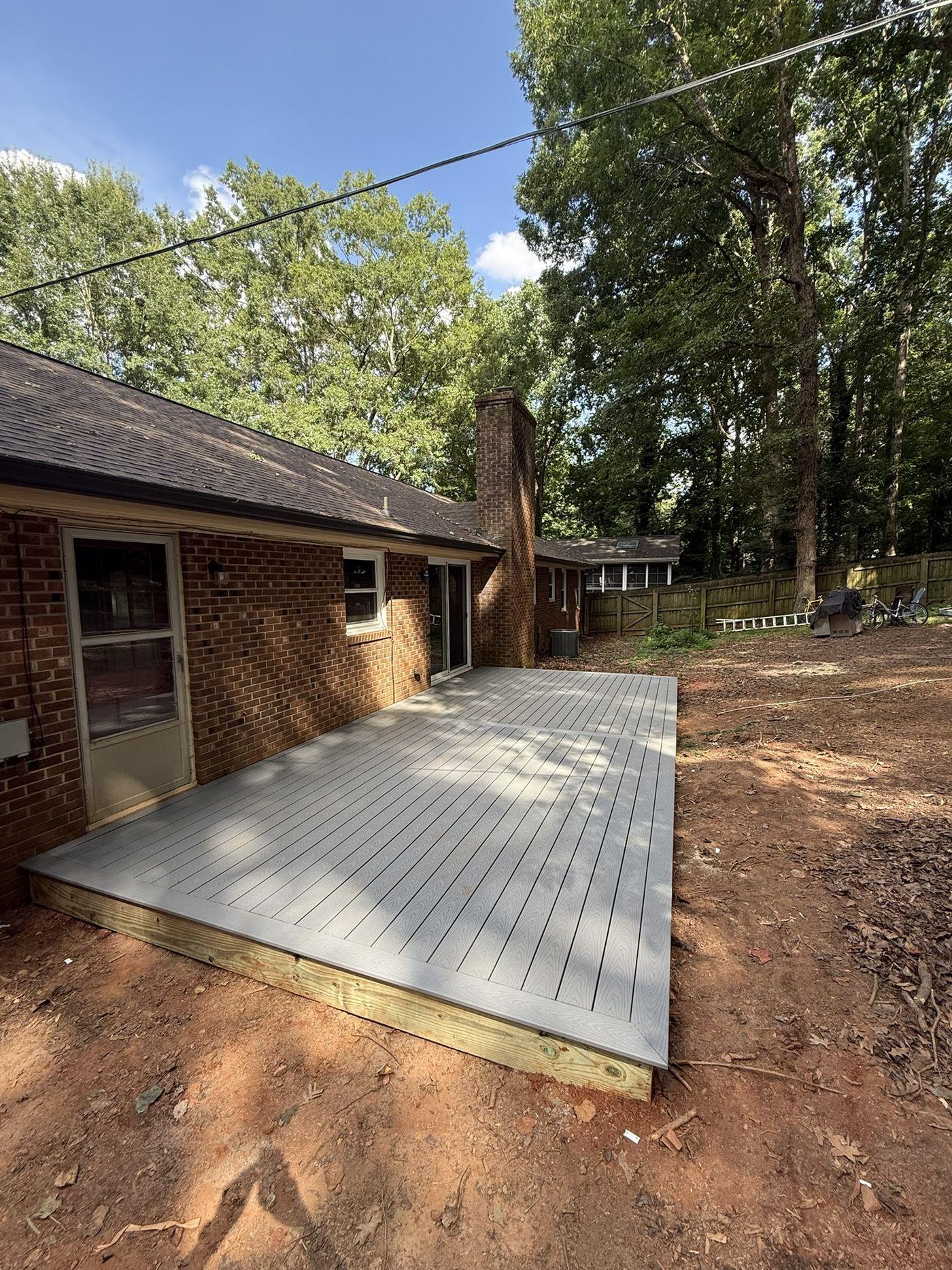 Completed grey composite deck built along the rear of a brick ranch house