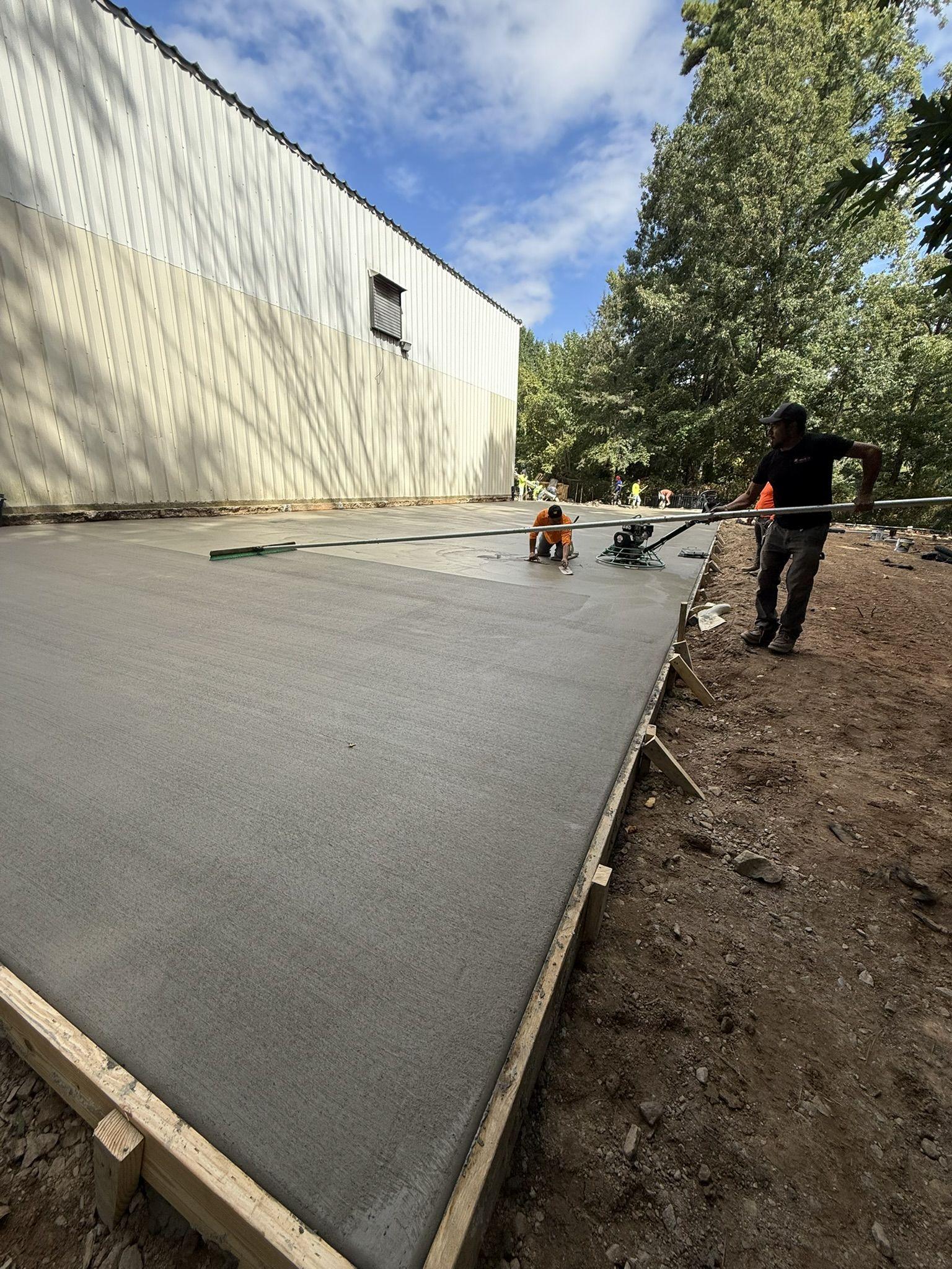 Crew screeding and floating a freshly poured commercial concrete slab alongside a metal building