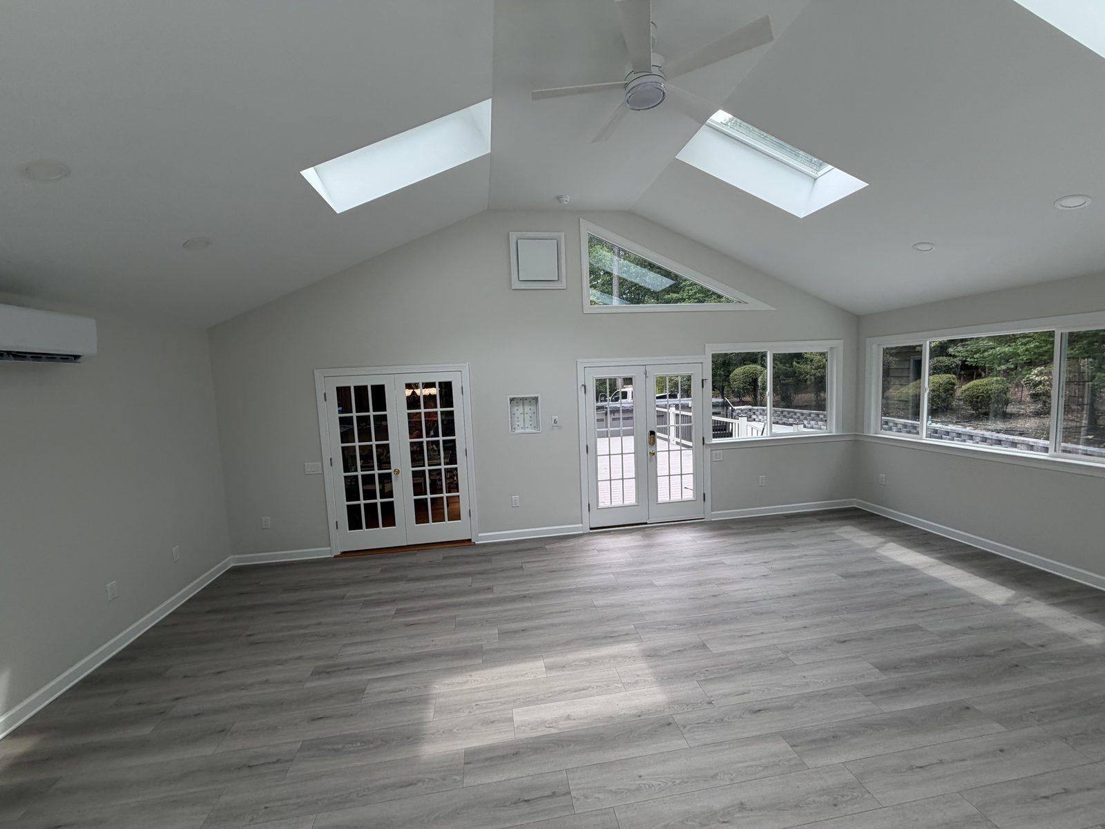 The finished sunroom interior with a vaulted ceiling, skylights, plank flooring and a wall-mounted heat pump head