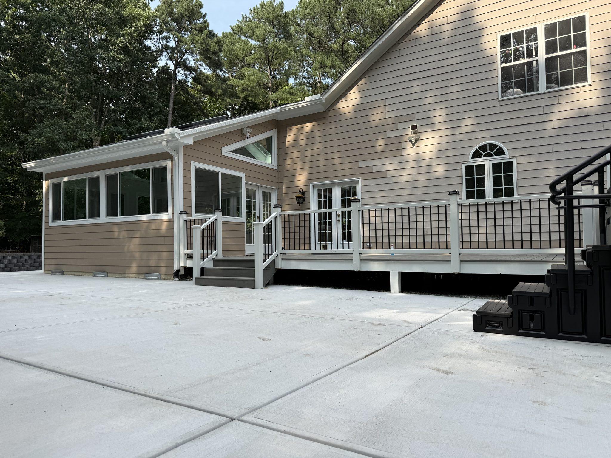 The completed rear elevation with the new sunroom, rebuilt deck and a wide concrete patio below — Arthur Sunroom & Backyard Transformation