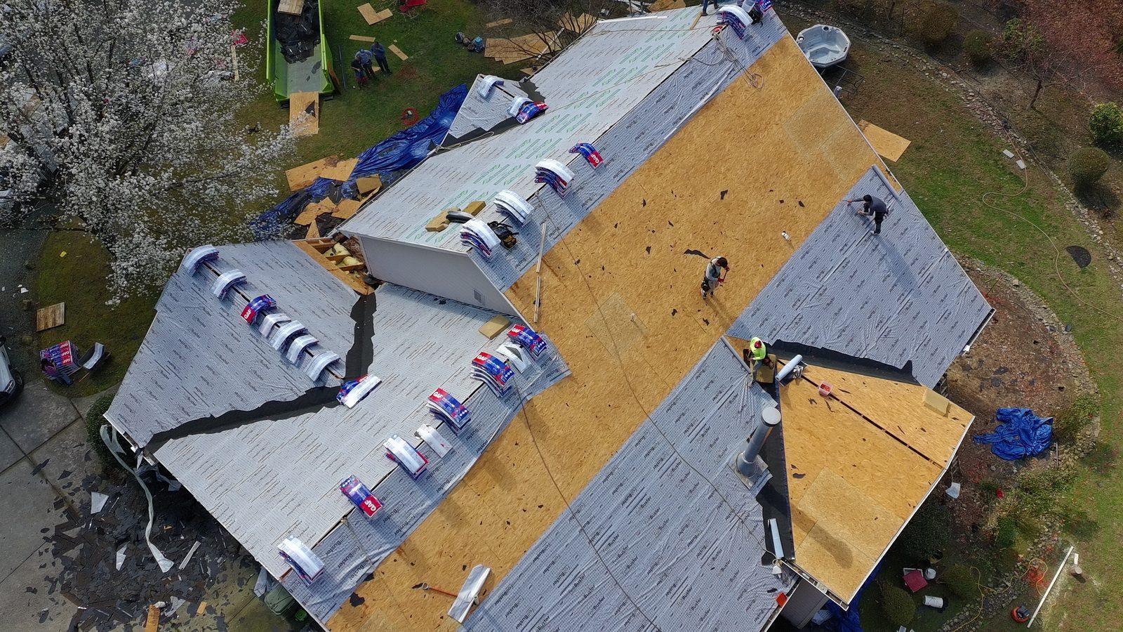 Aerial view of the roof mid-replacement with underlayment down and shingle bundles staged across the slope
