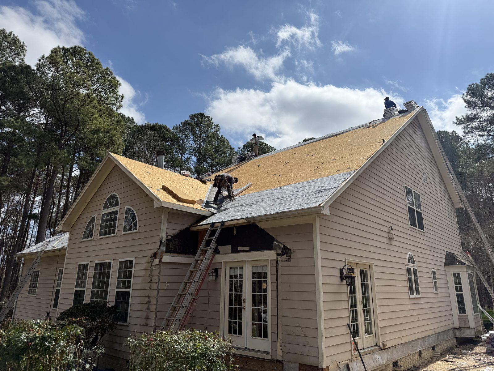 The roof stripped to bare decking with new sheathing going down and the crew working the ridge
