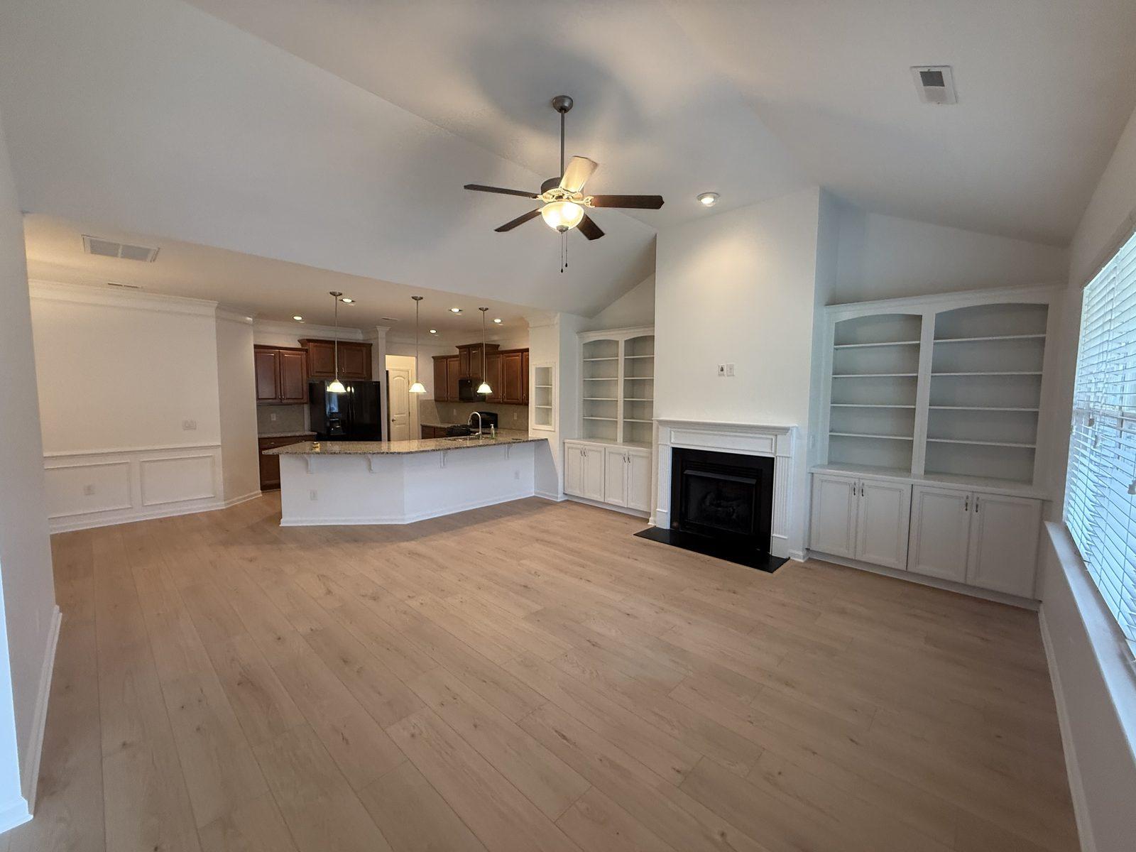 The same great room with the new light wide-plank floor fitted around the existing fireplace and built-ins
