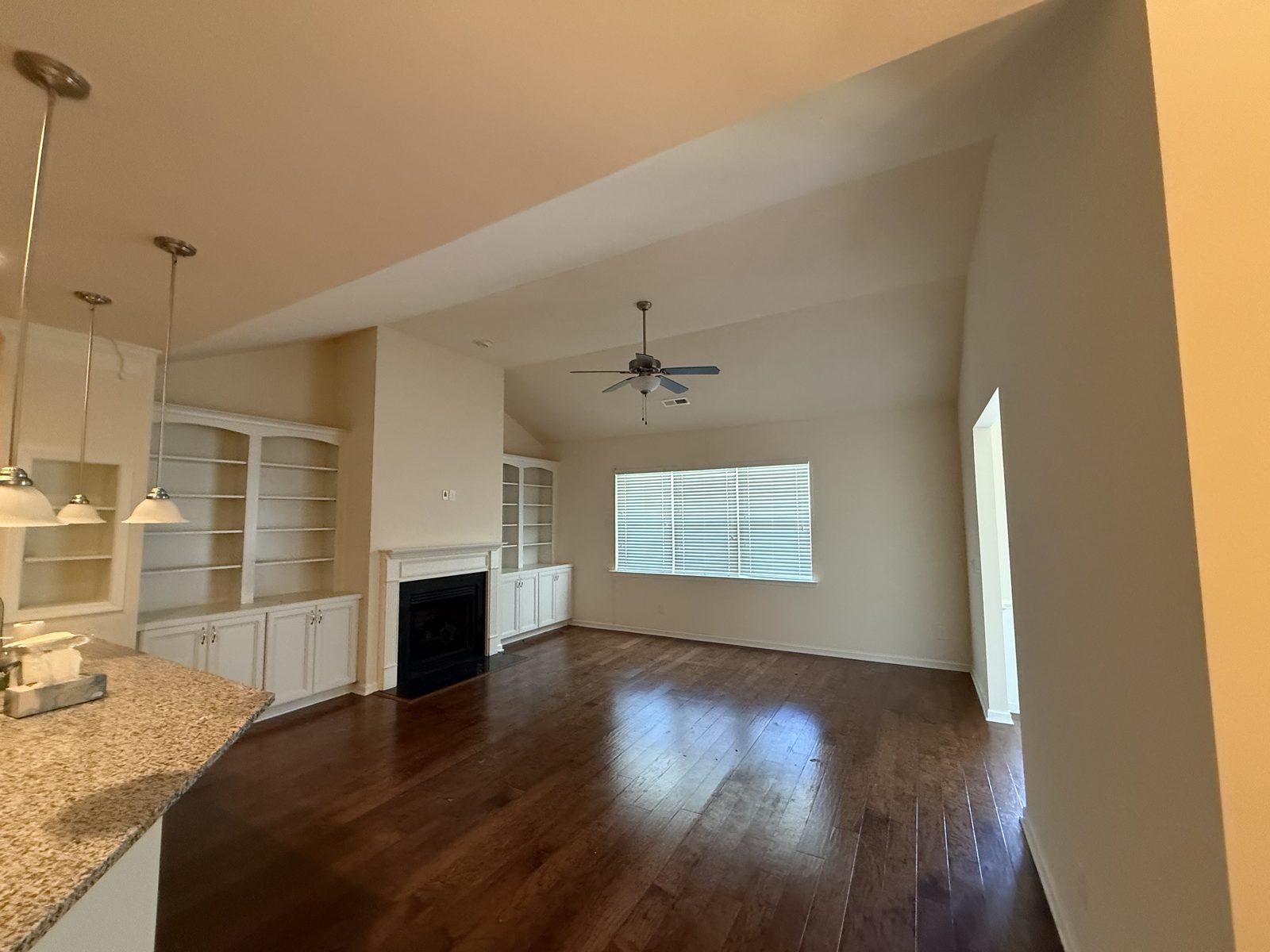 The great room before work, with dark stained hardwood running up to the fireplace and built-in shelving