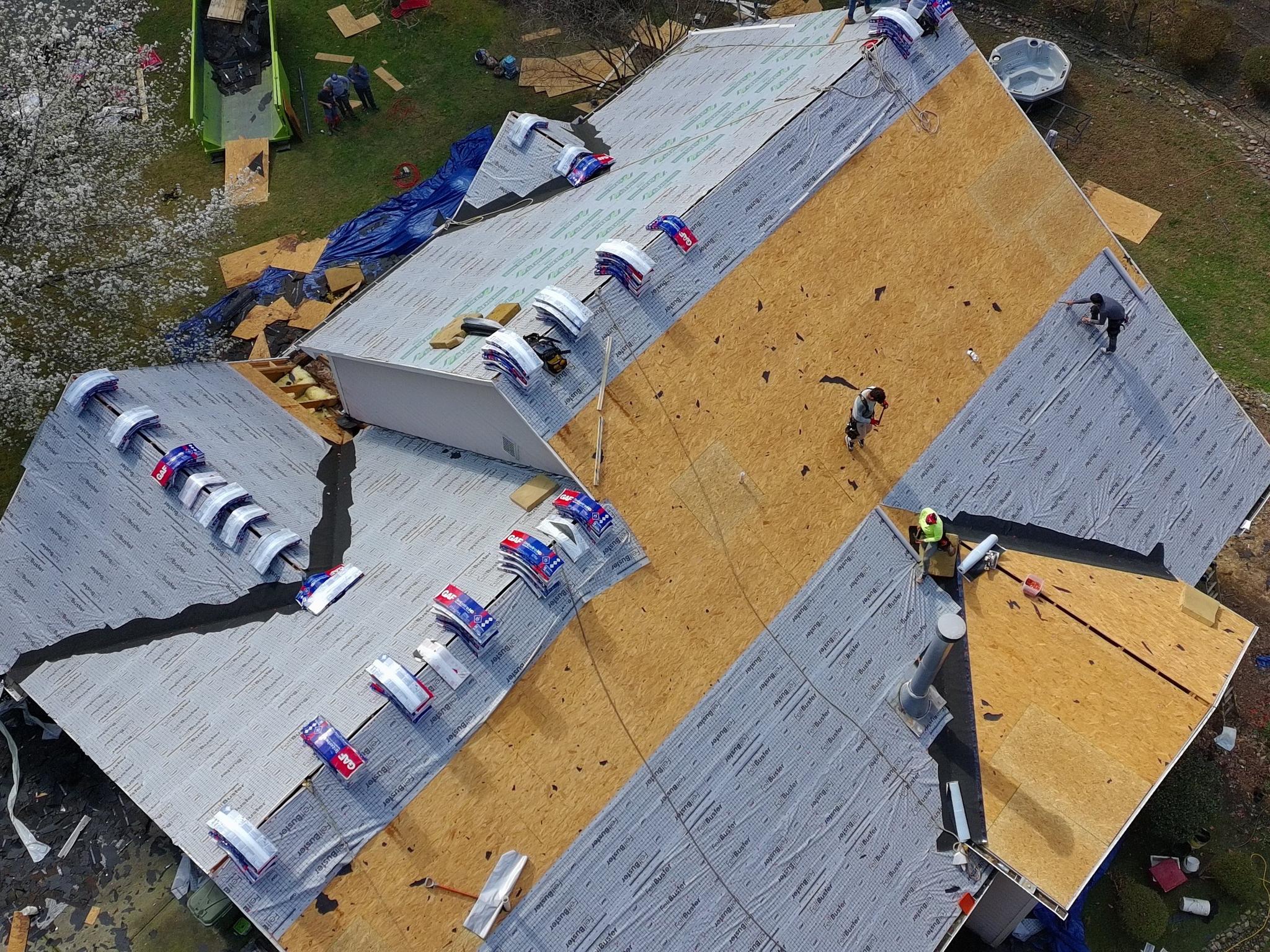 Aerial view of the roof mid-replacement, stripped to the decking with new underlayment down and the crew working across the slope — Arthur Sunroom & Backyard Transformation