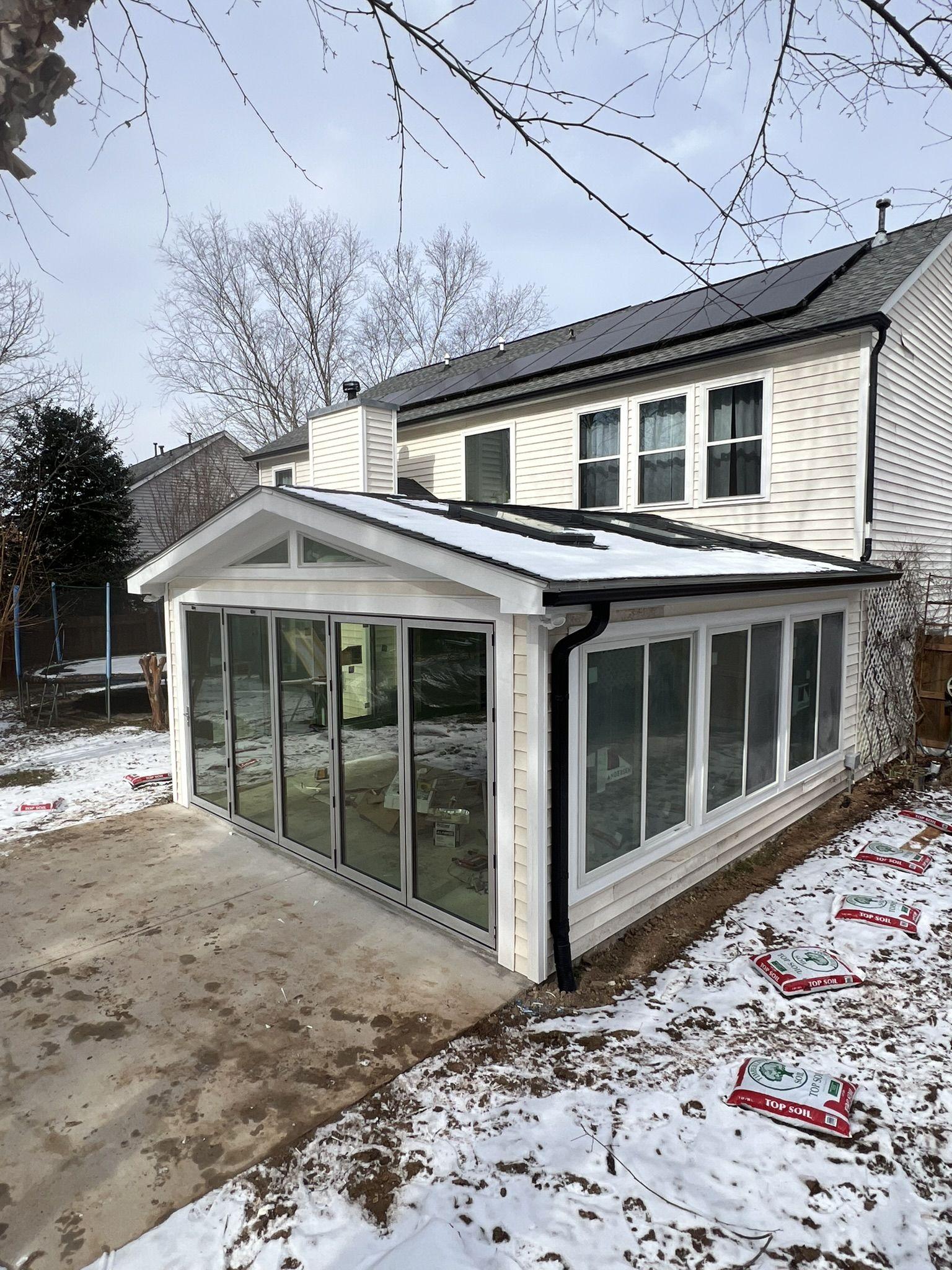 Completed glazed sunroom addition with a gabled roof on the rear of a two-storey home in winter