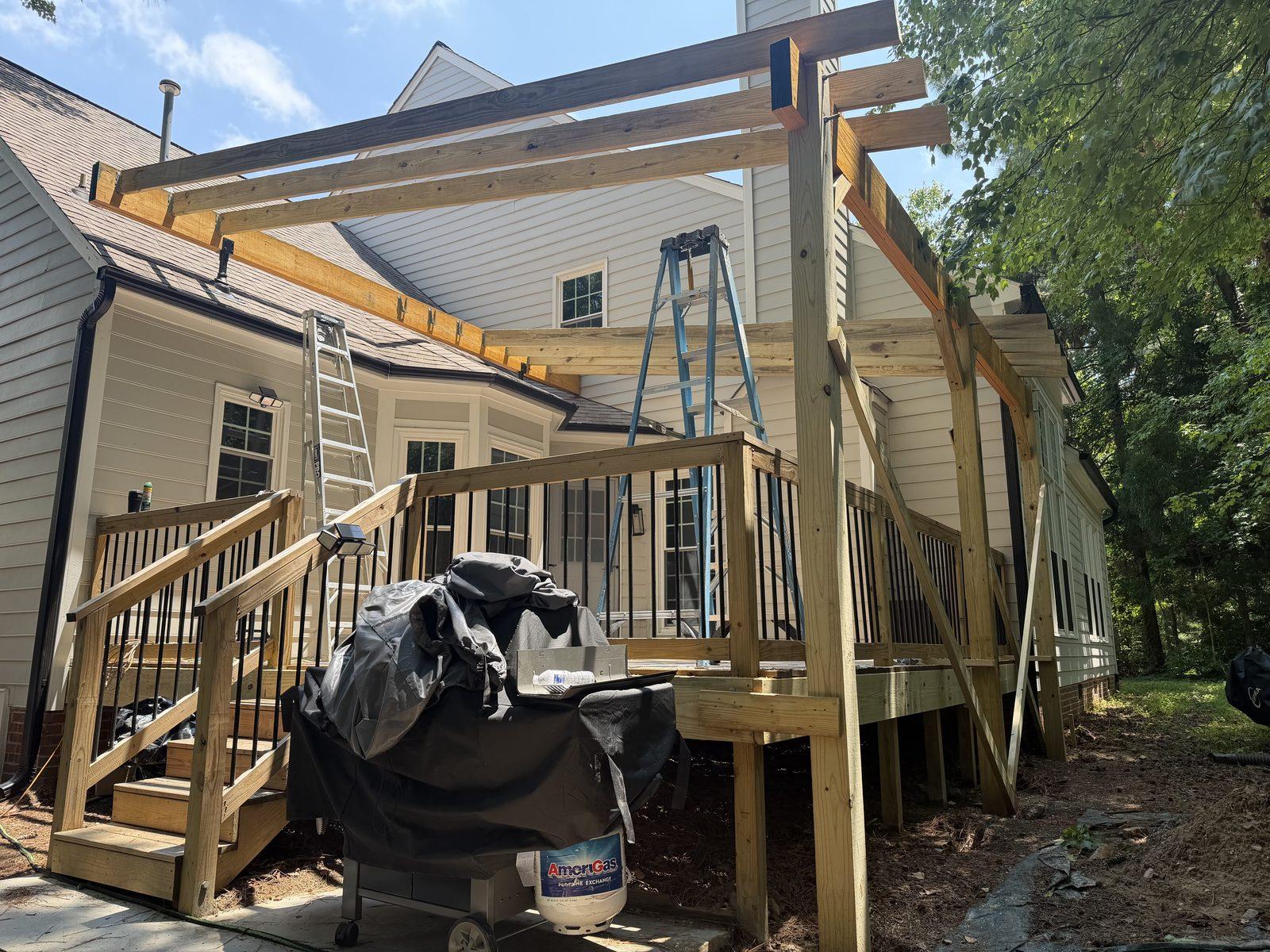 The pergola part-built, with posts and beams up and rafters being set from a ladder