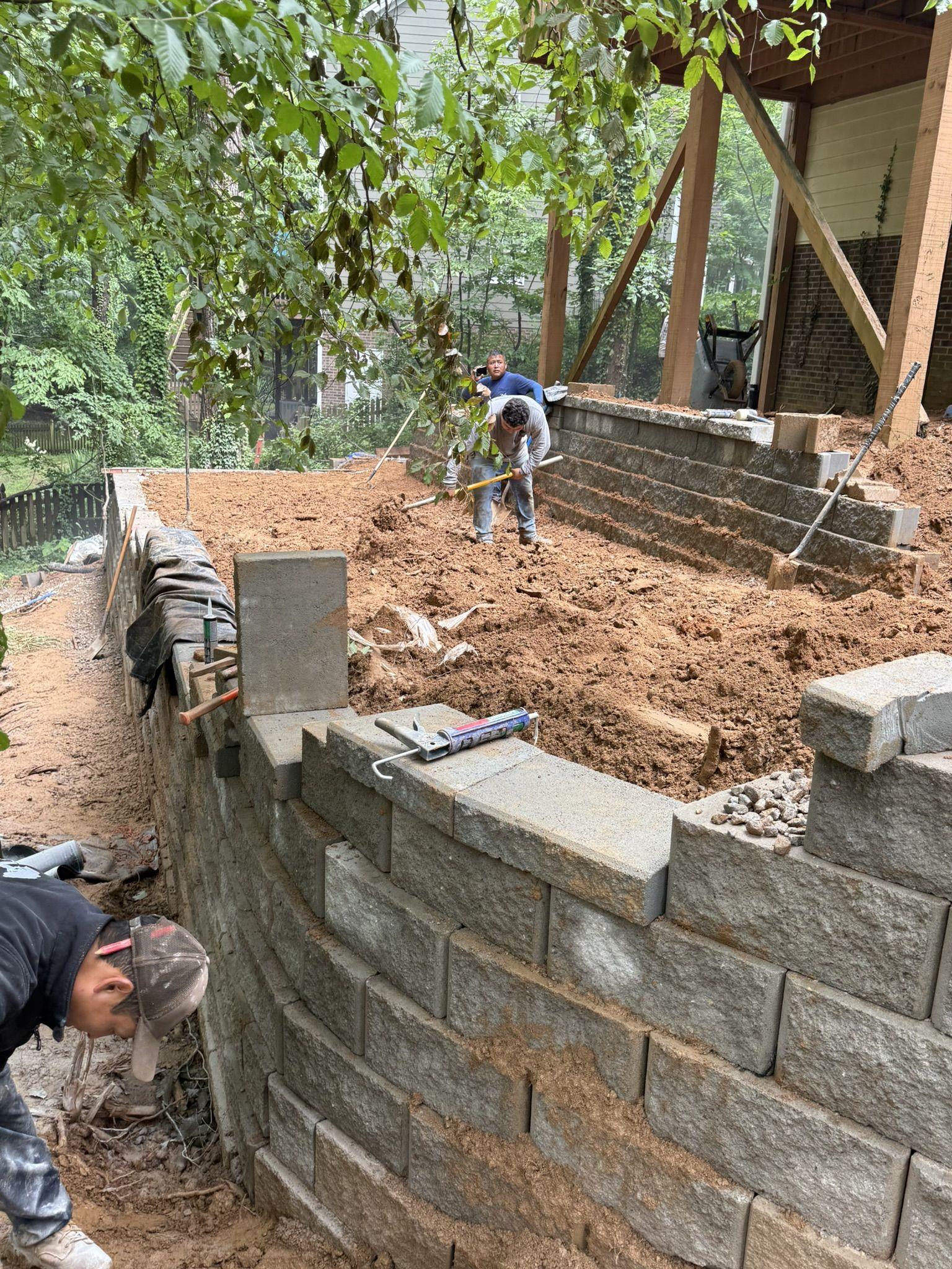 Segmental block retaining wall being laid course by course into a cut slope behind a house