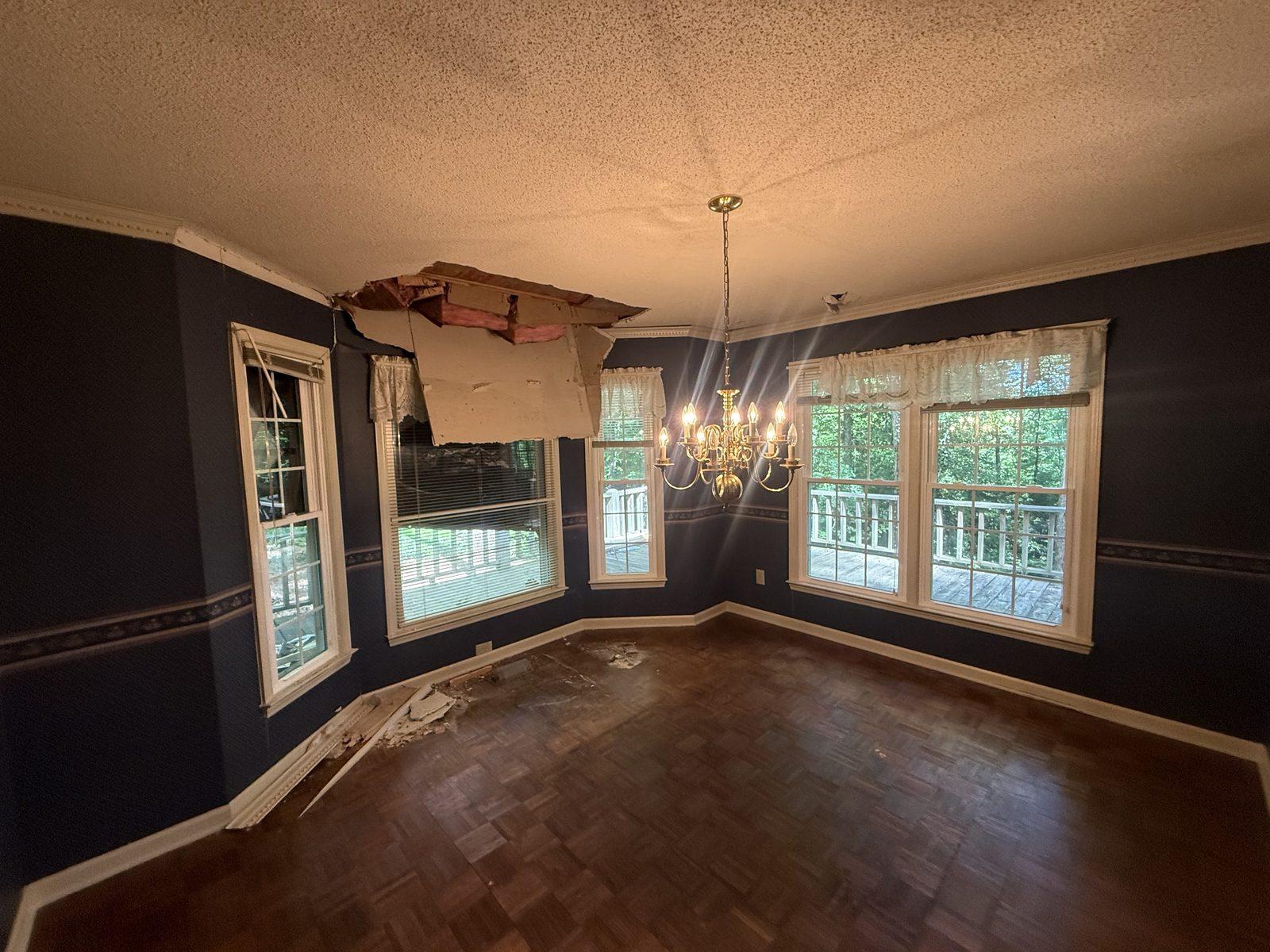 The dining room after the impact, with the ceiling torn open to the insulation above and debris across the parquet floor