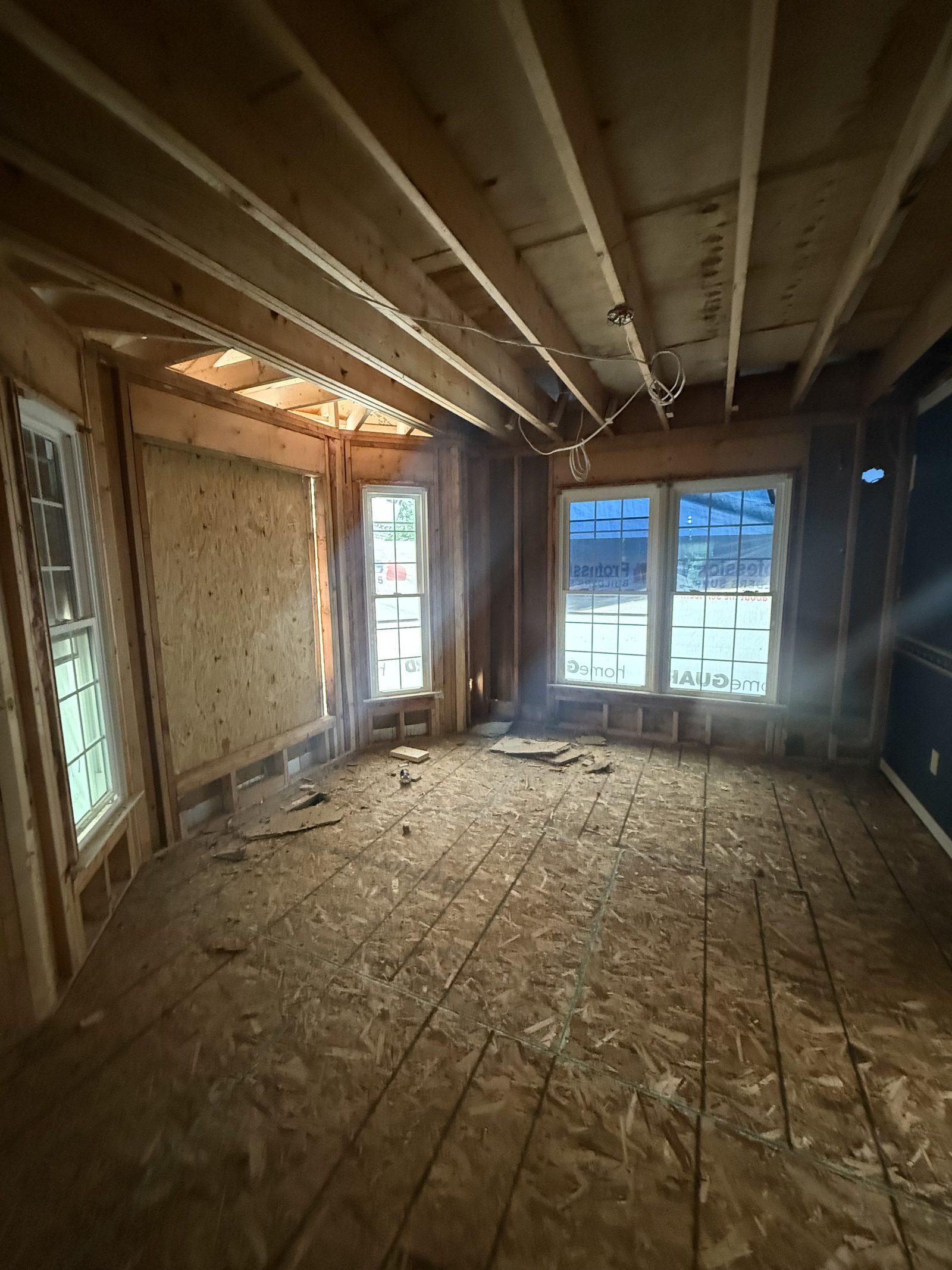 The interior taken back to studs and rafters, with new framing in place and the subfloor exposed