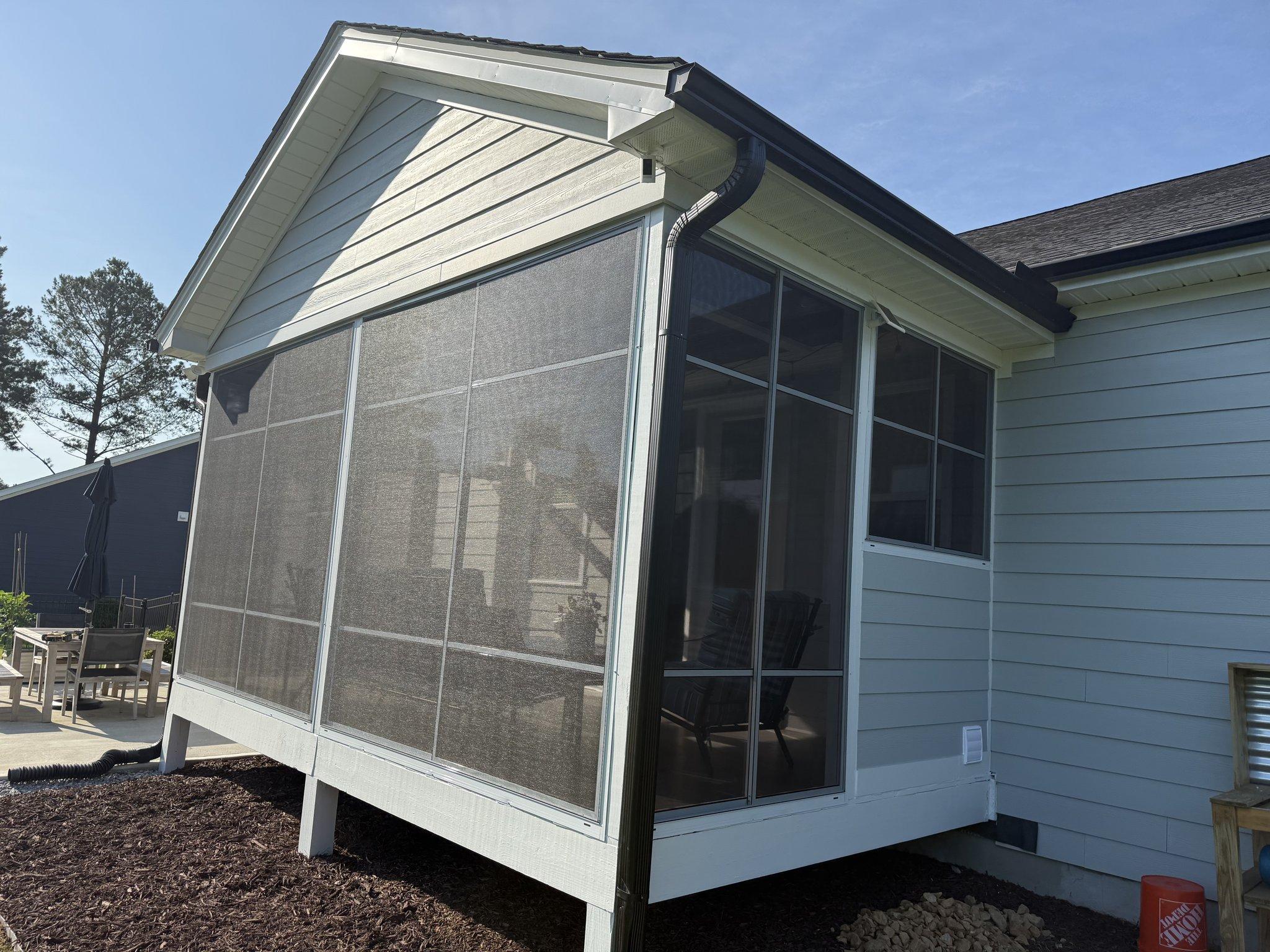 The finished three-season room from the corner, its screened panels framed in white beneath the gable, with the new deck below