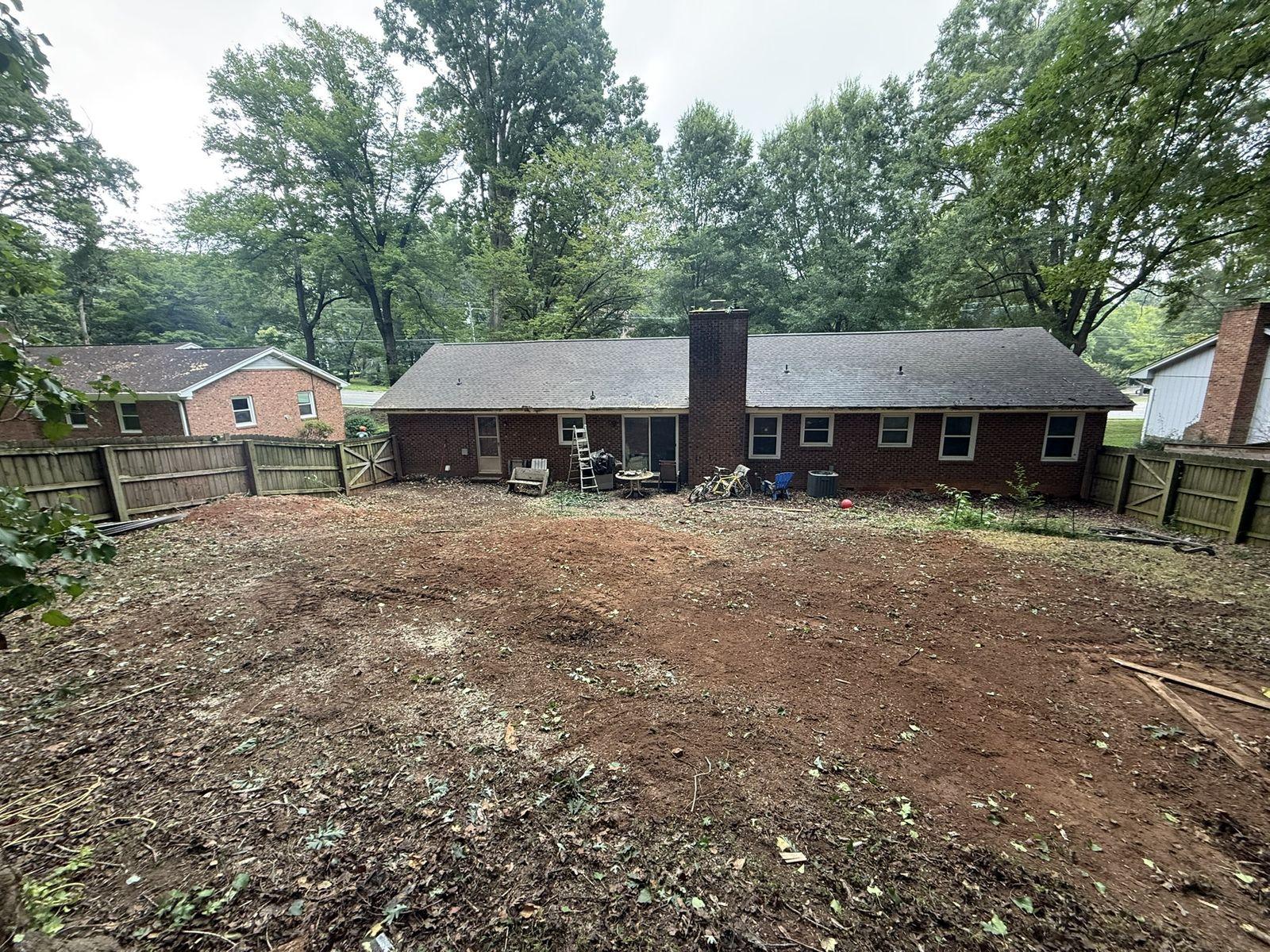 Bare graded soil across the rear yard of a brick ranch house before deck construction
