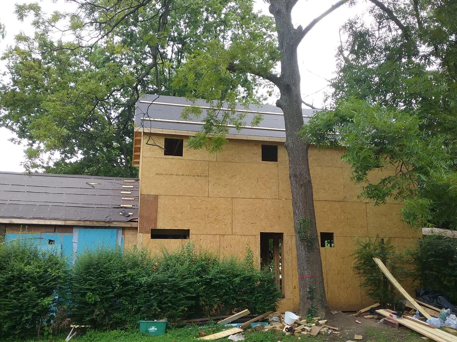 A whole-house renovation mid-build, the exterior stripped and sheathed with the crew working from ladders — Cabarrus Custom Flip