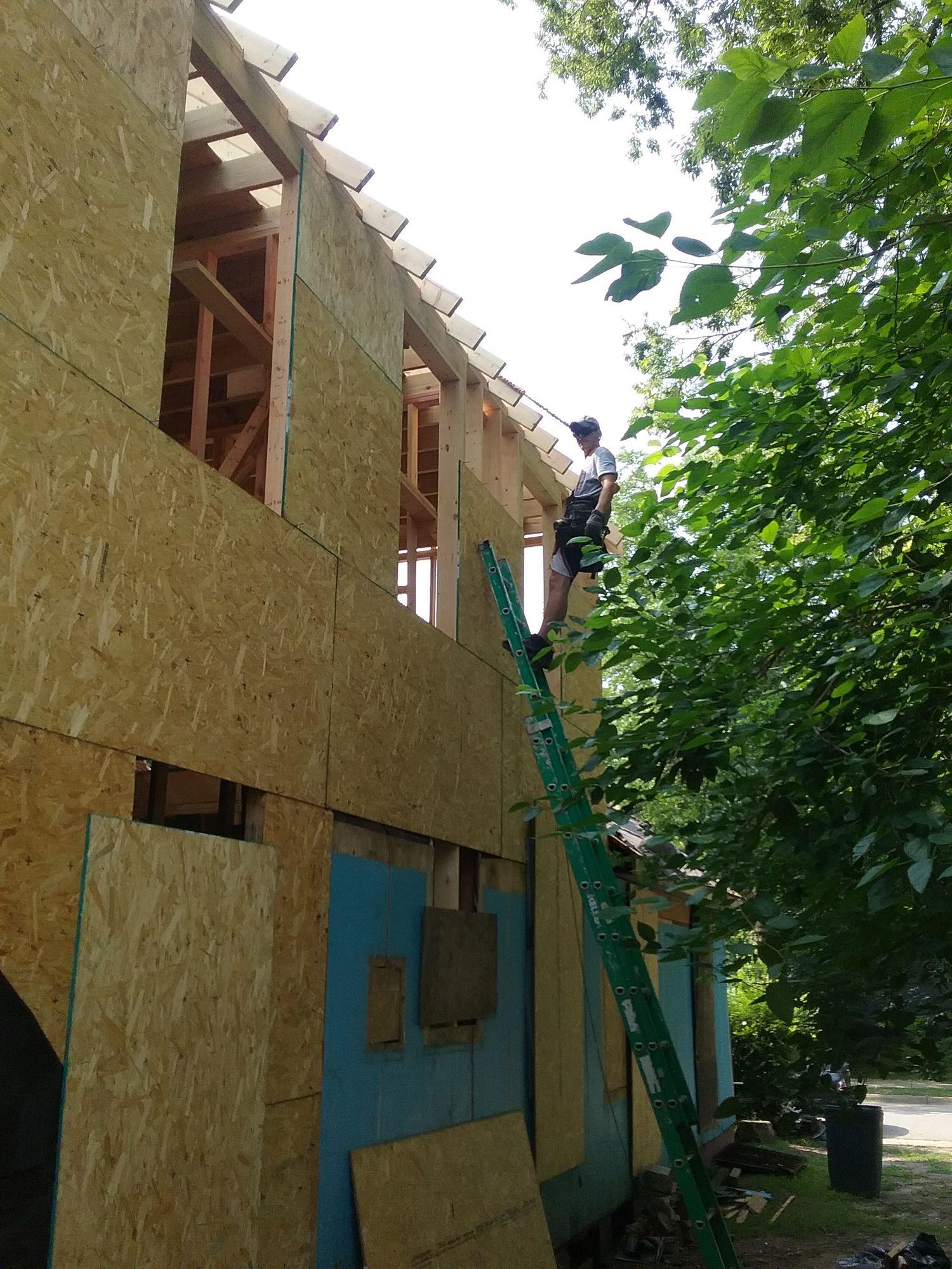 Worker on a ladder against the sheathed two-storey elevation during the renovation