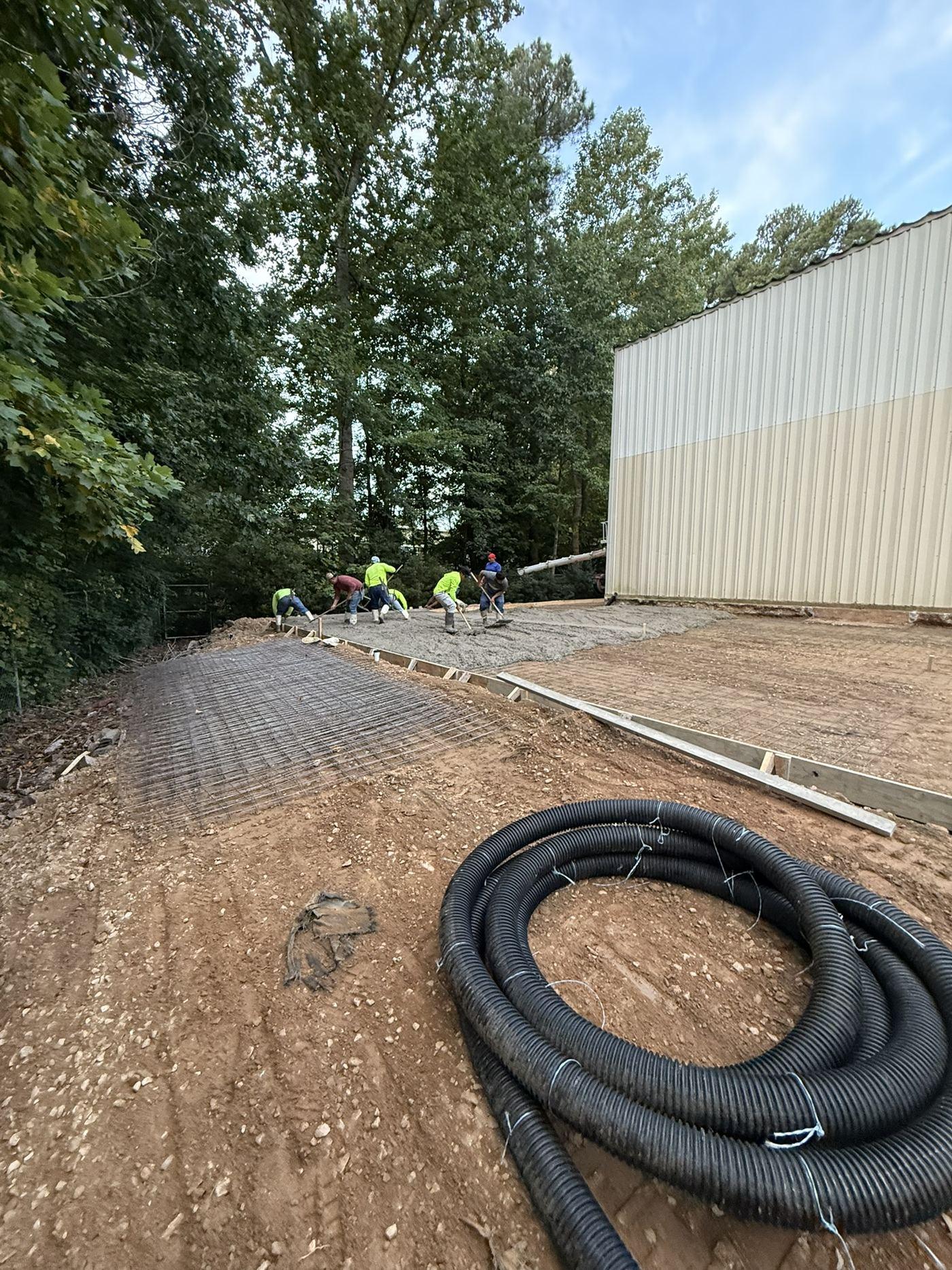 Graded ground with drainage pipe laid out and crew working alongside the commercial building