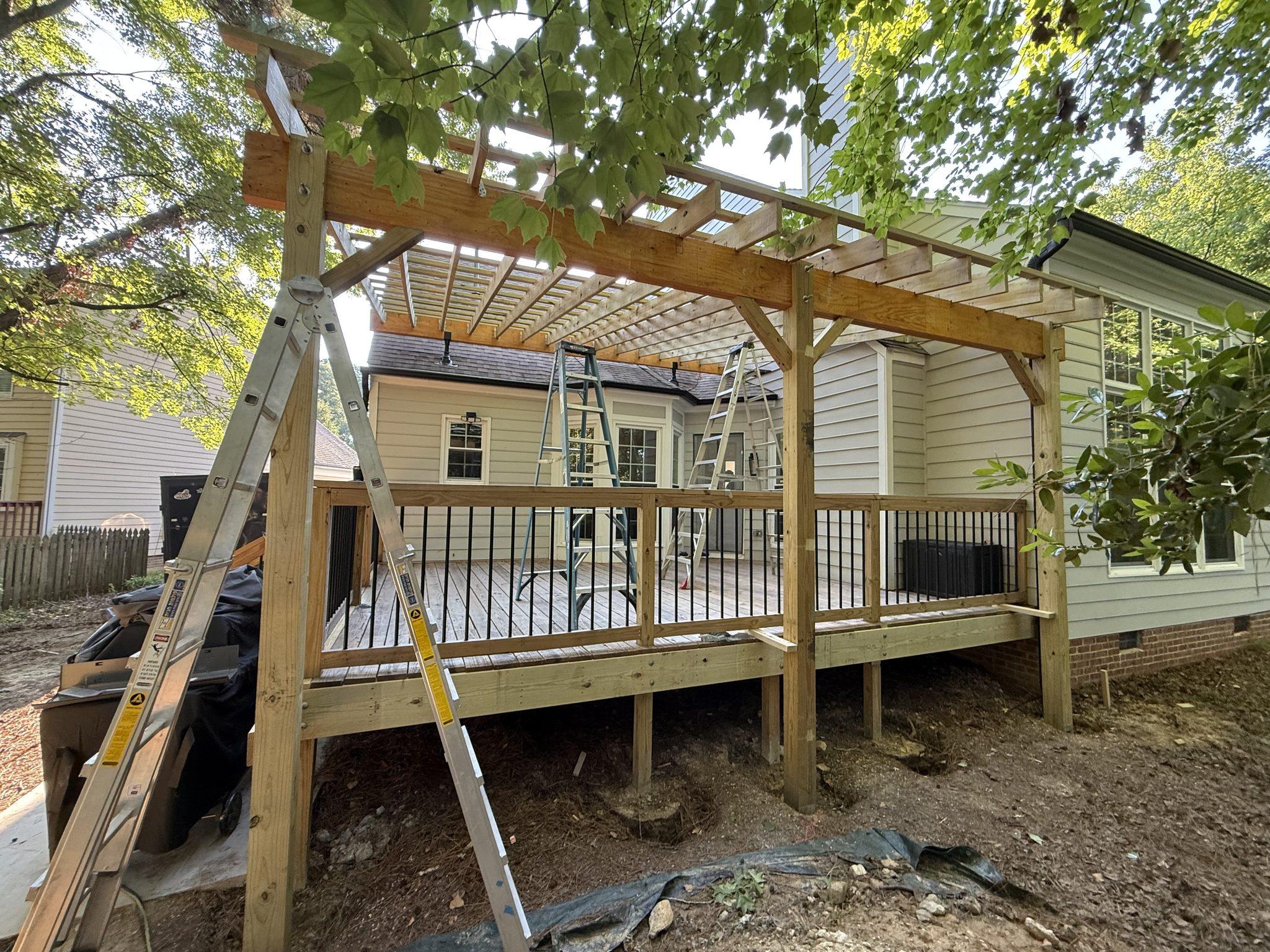 The completed timber pergola standing over the raised rear deck, with the crew finishing from ladders — Dennis Pergola Addition