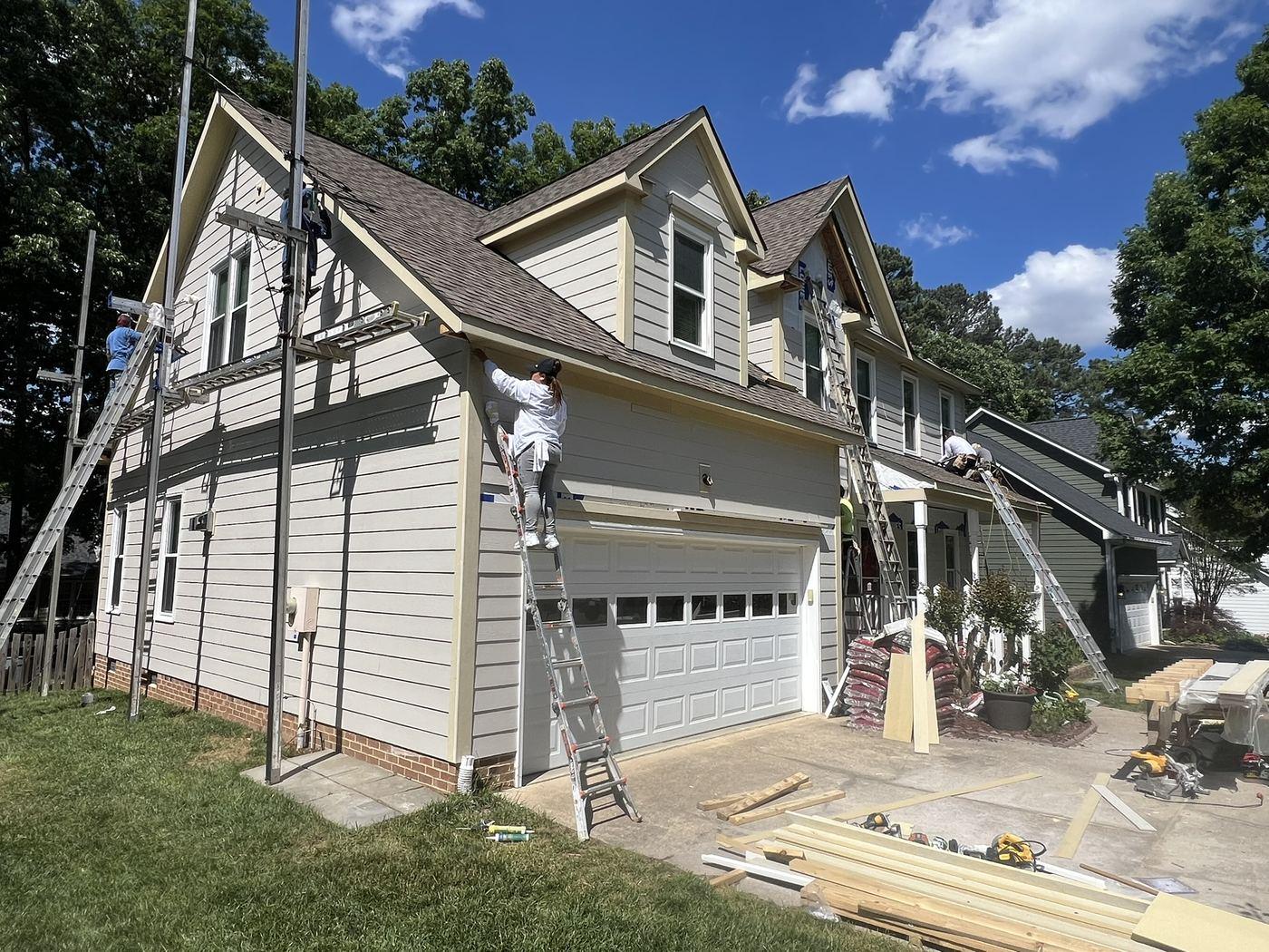 Crew installing new siding over housewrap from ladders across the front elevation of a house