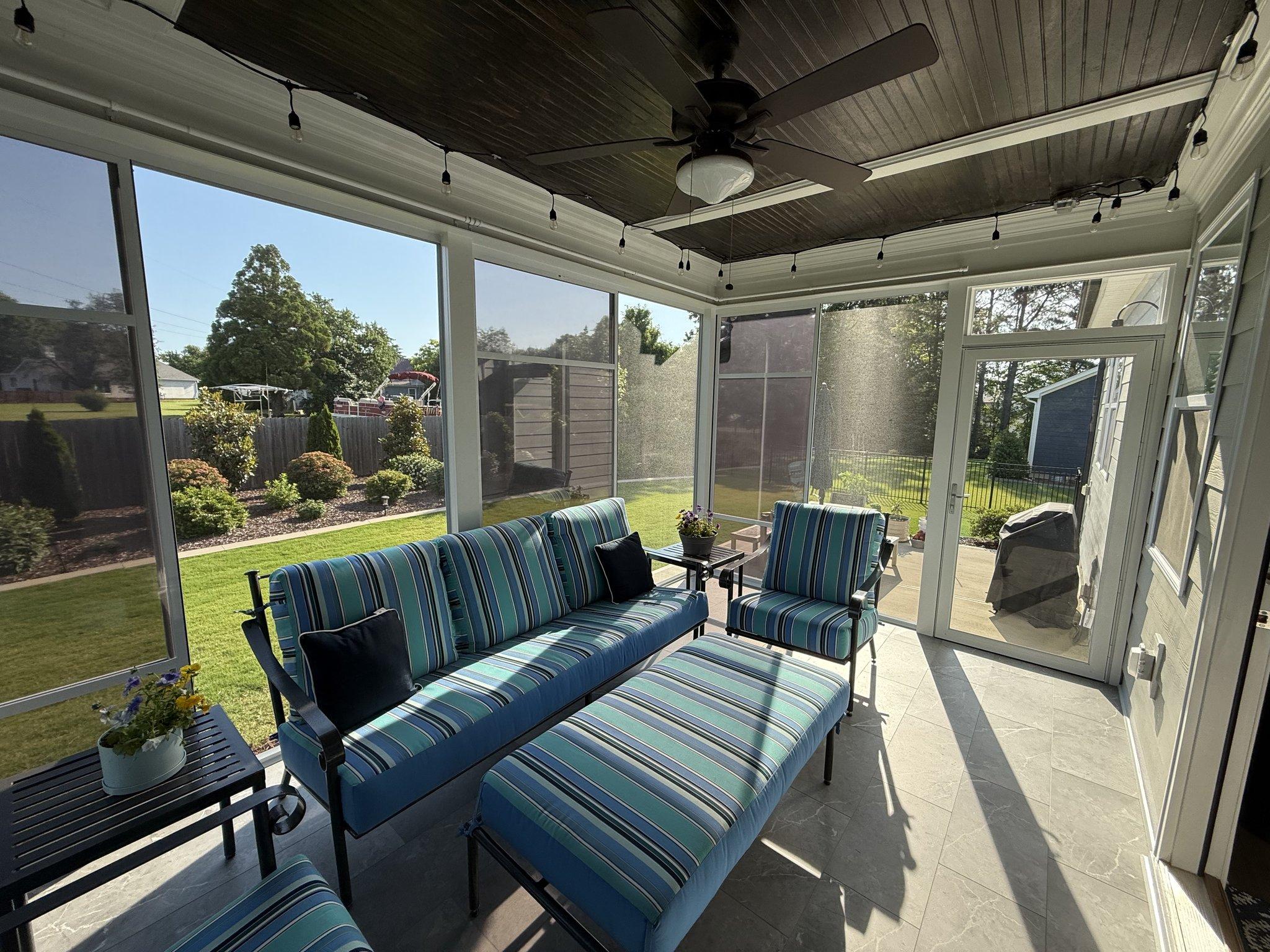 Inside the finished screened room: striped outdoor seating, a dark finished ceiling with a fan and string lights
