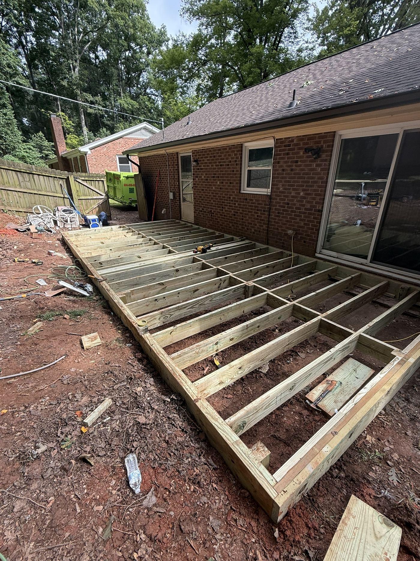 Pressure-treated joists framed across the deck footprint against the rear wall of the house